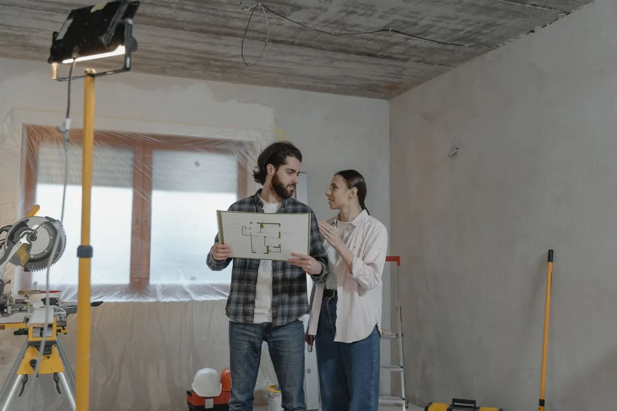 Two people holding drawings in a room mid-renovation